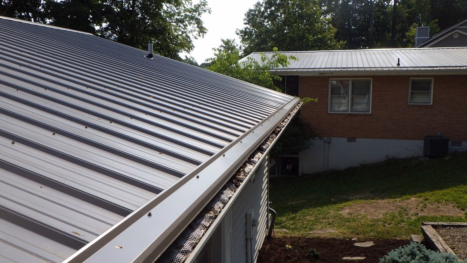 Gray standing-seam metal roof with a new gutter running along the eave