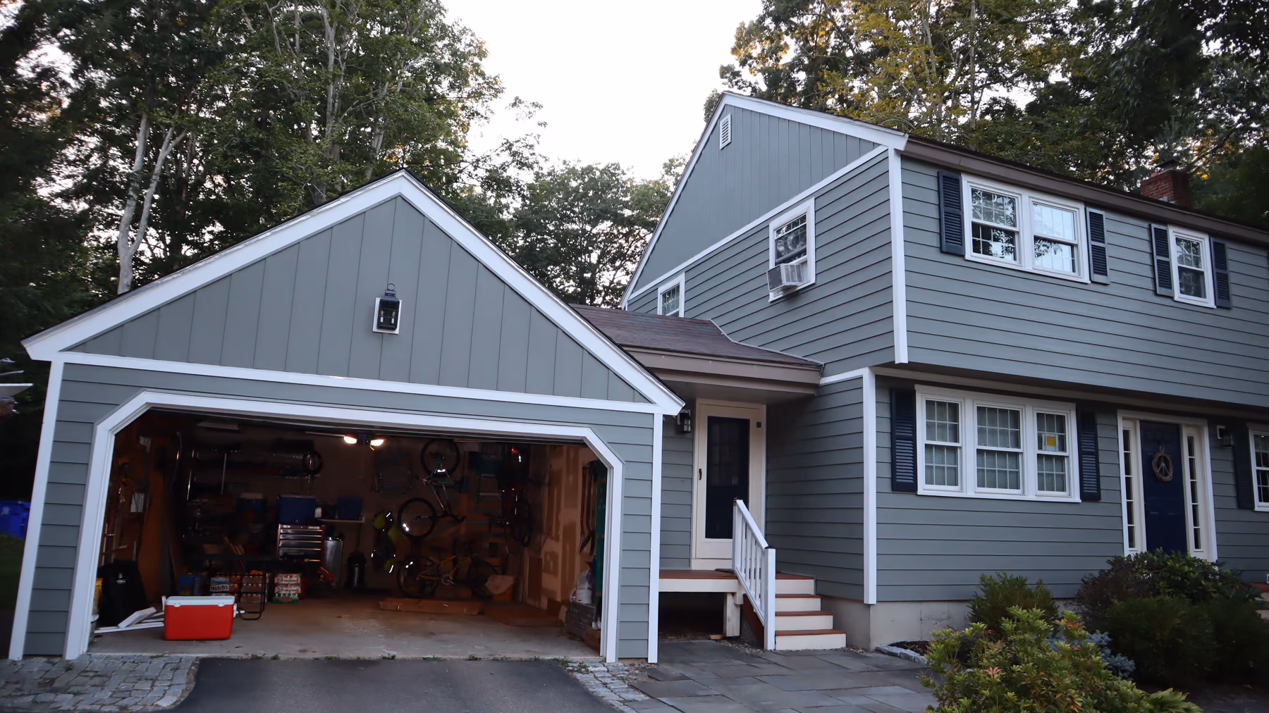 Attached two-car garage clad in green vinyl siding with white board-and-batten gable and white trim