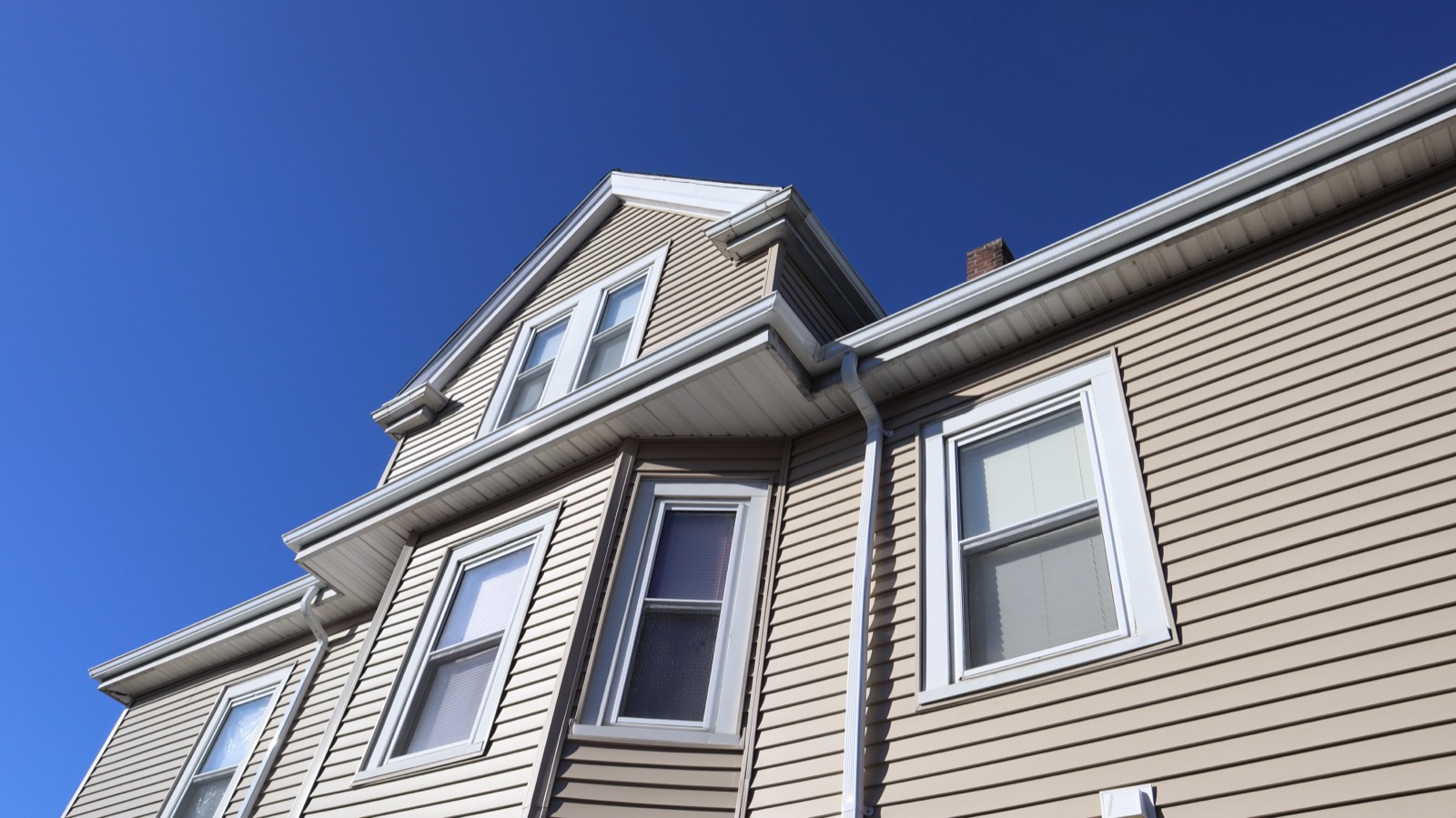 Upward view of a dormer and trim work in new siding against a vivid blue sky