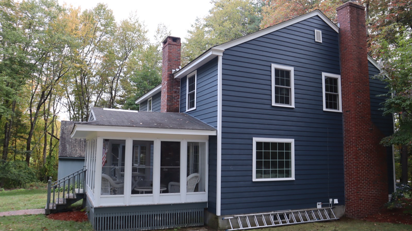 Navy siding with a prominent brick chimney and a screened porch in a wooded setting
